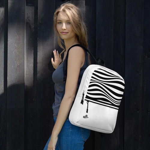 A woman wearing a gray tank top and blue jeans carries a white backpack with a bold black wavy stripe pattern on the upper half, standing against a dark wooden plank wall.